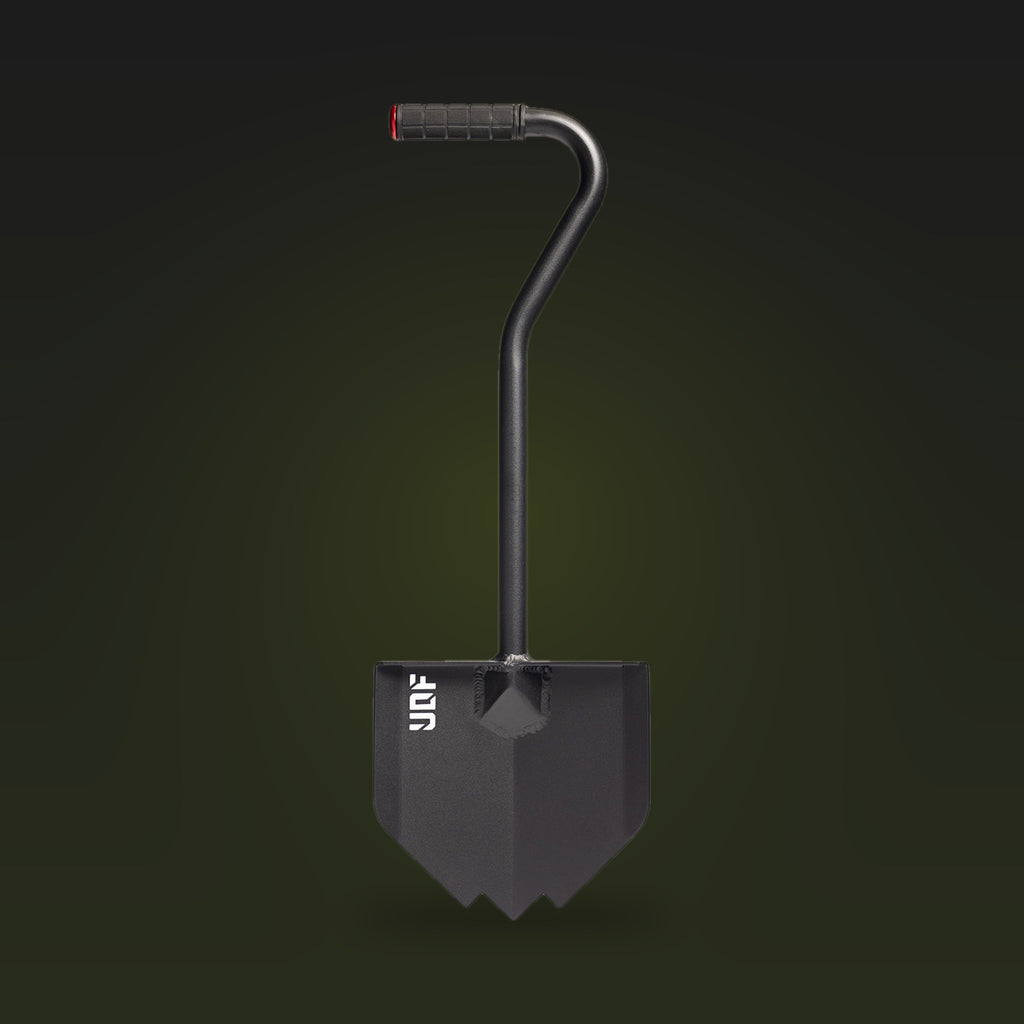 Black overland shovel with a pointed blade, bent handle and rubber grip, on a dark olive background
